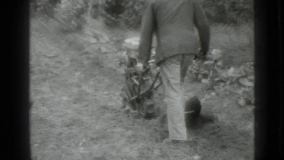 A man stands in the dirt holding the tiller handle, seen from behind in grainy black-and-white 8mm footage from the supplied Moscow setting.