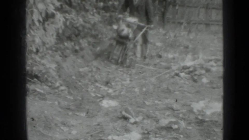 Black-and-white home-movie frame from Moscow, 1975, with a man positioned behind a hand tractor in a rough cultivated area.