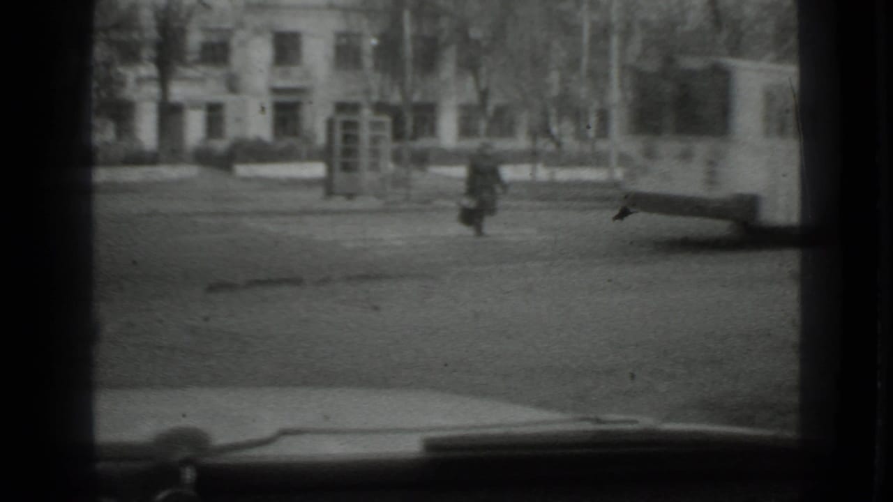 Distant woman walking across an open street seen through a vehicle window.