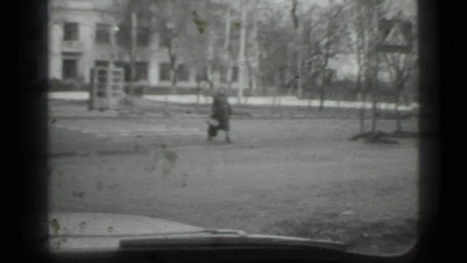 Moscow 1975 frame with a woman walking across the street near a roadside sign and sparse winter trees.