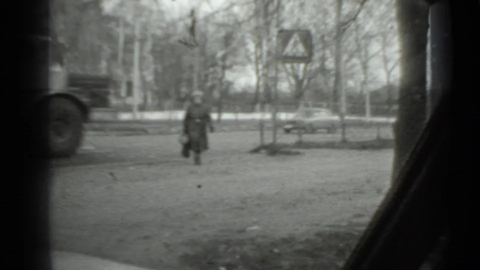 Moscow 1975 frame showing a woman crossing while a large vehicle and a smaller car pass in the background.