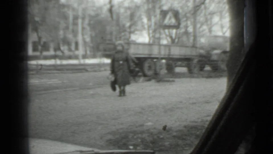 1975 Moscow frame of a woman in cold-weather clothing walking past a trailer, with bare trees and a pedestrian sign behind her.