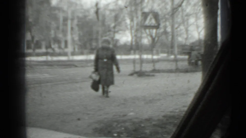 1975 Moscow home-movie view of a woman carrying a handbag across a cold roadside area with a pedestrian sign and bare trees.
