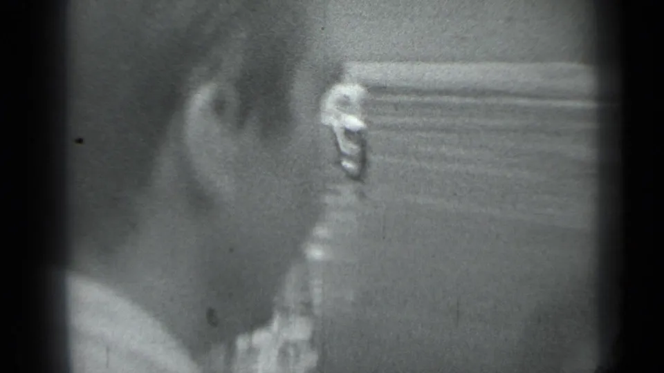 Black-and-white Moscow home-movie frame with a nearby person's head and shoulder beside a car, with street detail blurred in the background.