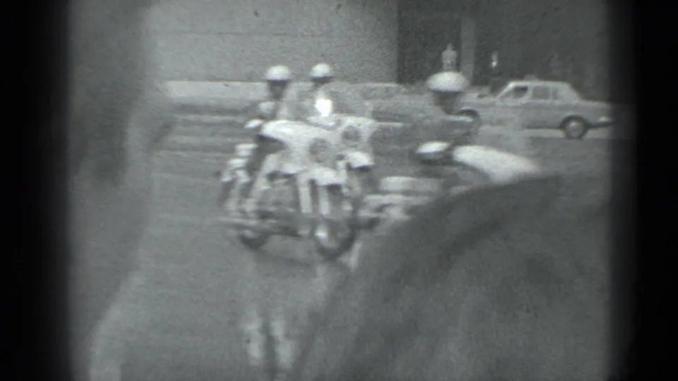 In supplied 1983 Moscow footage, helmeted motorcycle riders approach on a wide street as vintage cars pass in the background.