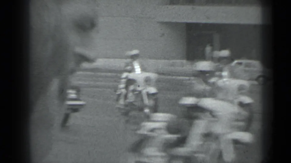 Helmeted motorcycle riders and boxy cars pass across the frame in monochrome 8mm footage identified as Moscow in 1983.