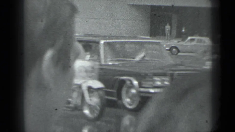A dark luxury-style sedan passes beside a motorcycle rider in the supplied 1983 Moscow street footage.