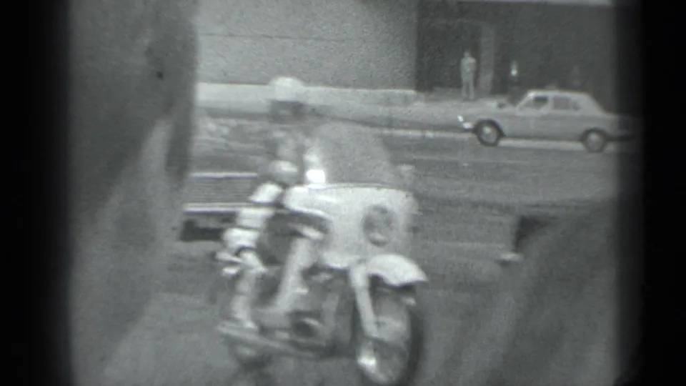 A close motorcycle rider passes through the foreground while vintage cars remain visible across the Moscow street.