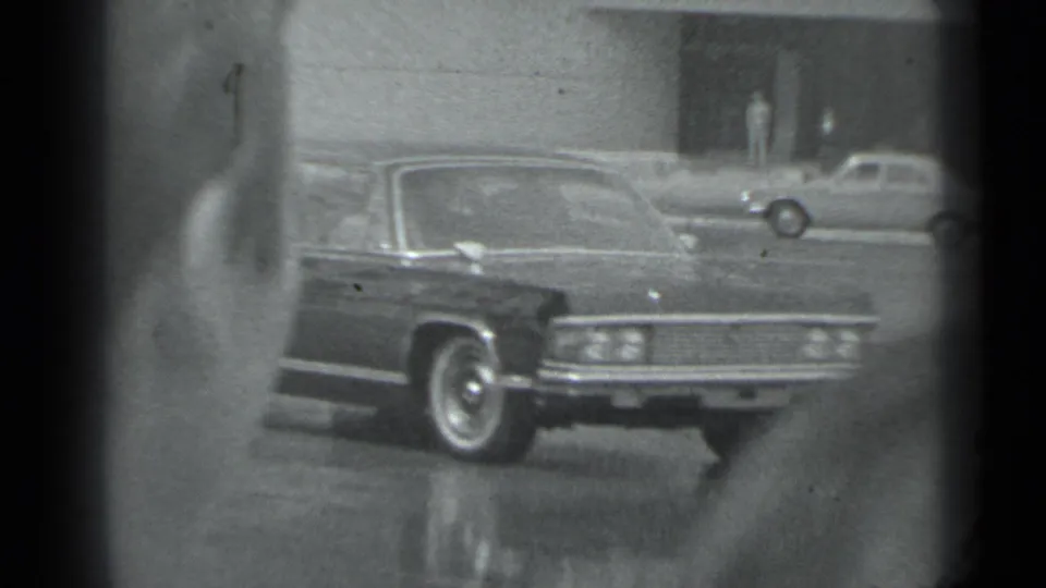 1983 Moscow 8mm frame showing a dark sedan with chrome trim on an urban street, seen through soft black-and-white home-movie framing.