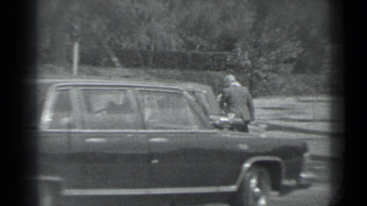 Dark sedan stopped near a curb with people standing nearby.