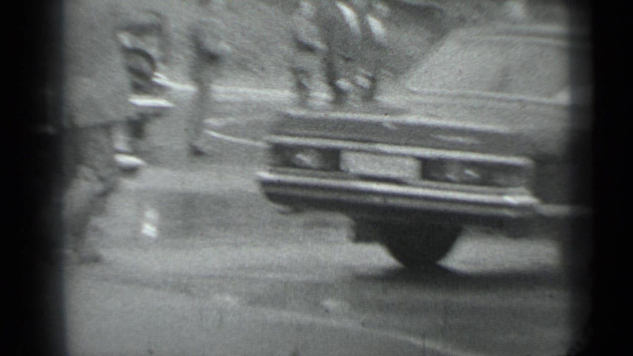 Blurred rear of a sedan with pedestrians and another vehicle in the background.