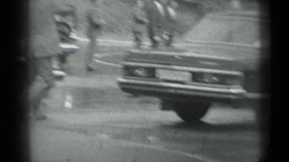 Soft 8mm frame from Moscow in 1983 with a sedan rear in the foreground and people moving beyond it.