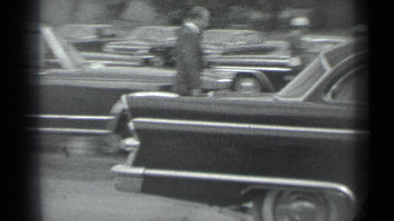 1983 Moscow 8mm frame showing a dark vintage sedan, parked cars, and suited figures partly obscured by film-frame edges.