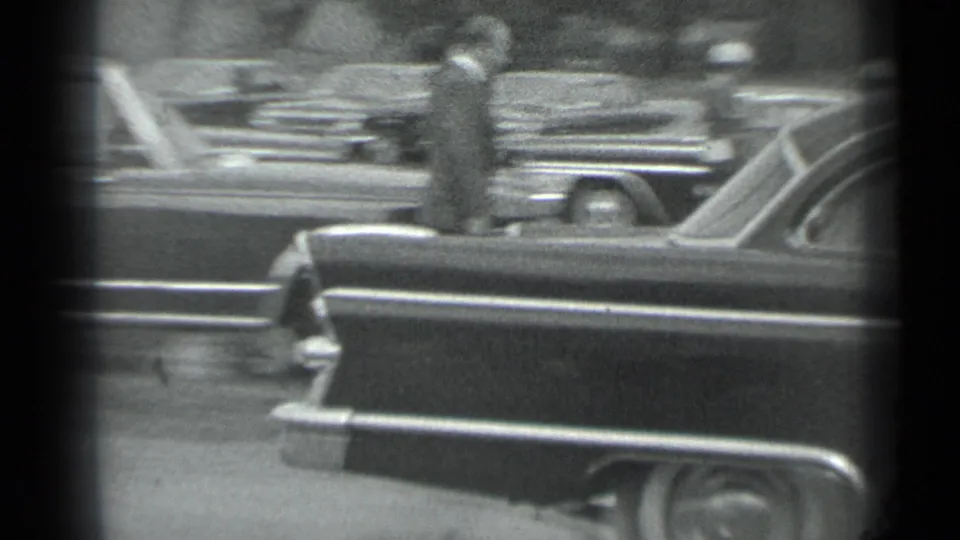 1983 Moscow 8mm frame showing a dark vintage sedan, parked cars, and suited figures partly obscured by film-frame edges.