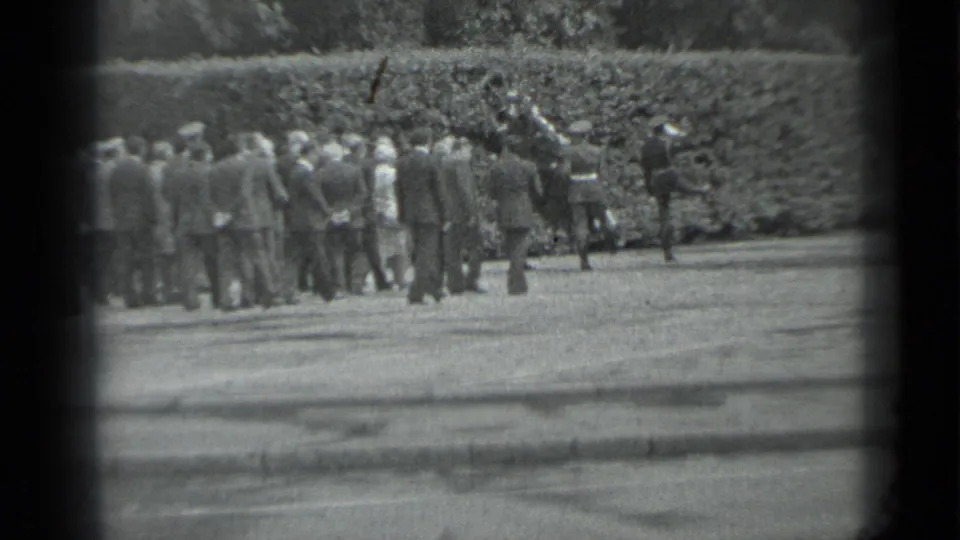 A clustered group of mourners moves along a paved Moscow path in the supplied 1983 funeral procession footage.