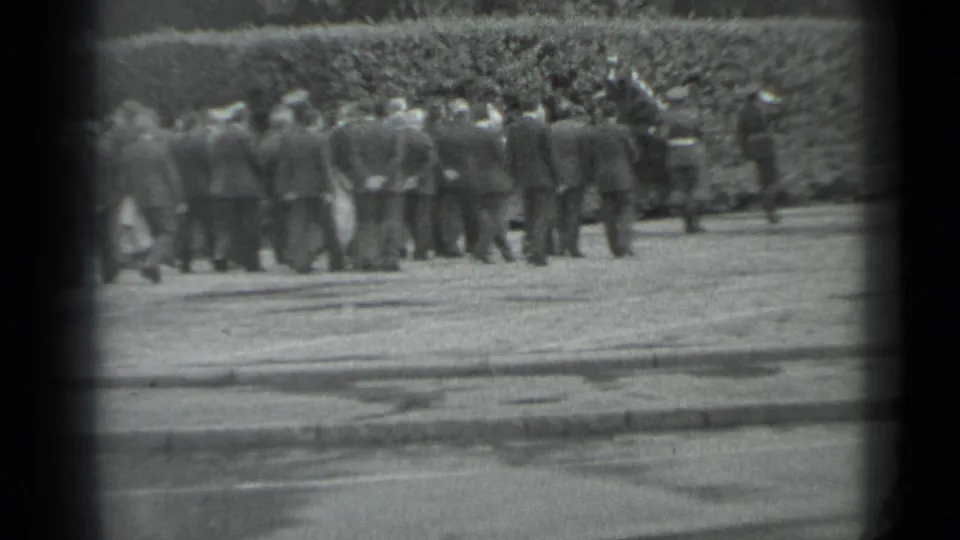 Black-and-white 8mm frame showing a dense group of formally dressed adults outdoors in Moscow, seen from a distance near a hedge.