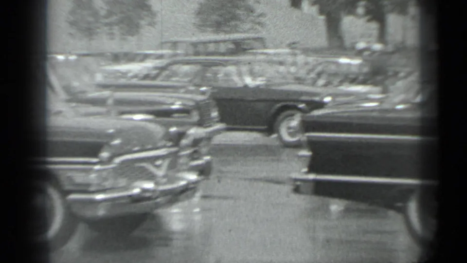 Black-and-white 8mm frame of a Moscow parking area with several older cars and prominent chrome-trimmed sedans in the foreground.