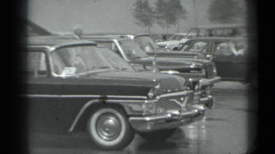 1983 Moscow home-movie frame showing classic sedans lined up outdoors, including a prominent dark car with chrome trim.
