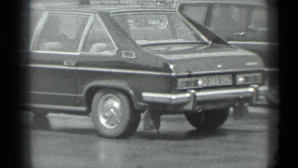 Black-and-white 8mm frame showing the rear side of a compact car at a Moscow outdoor automotive display.