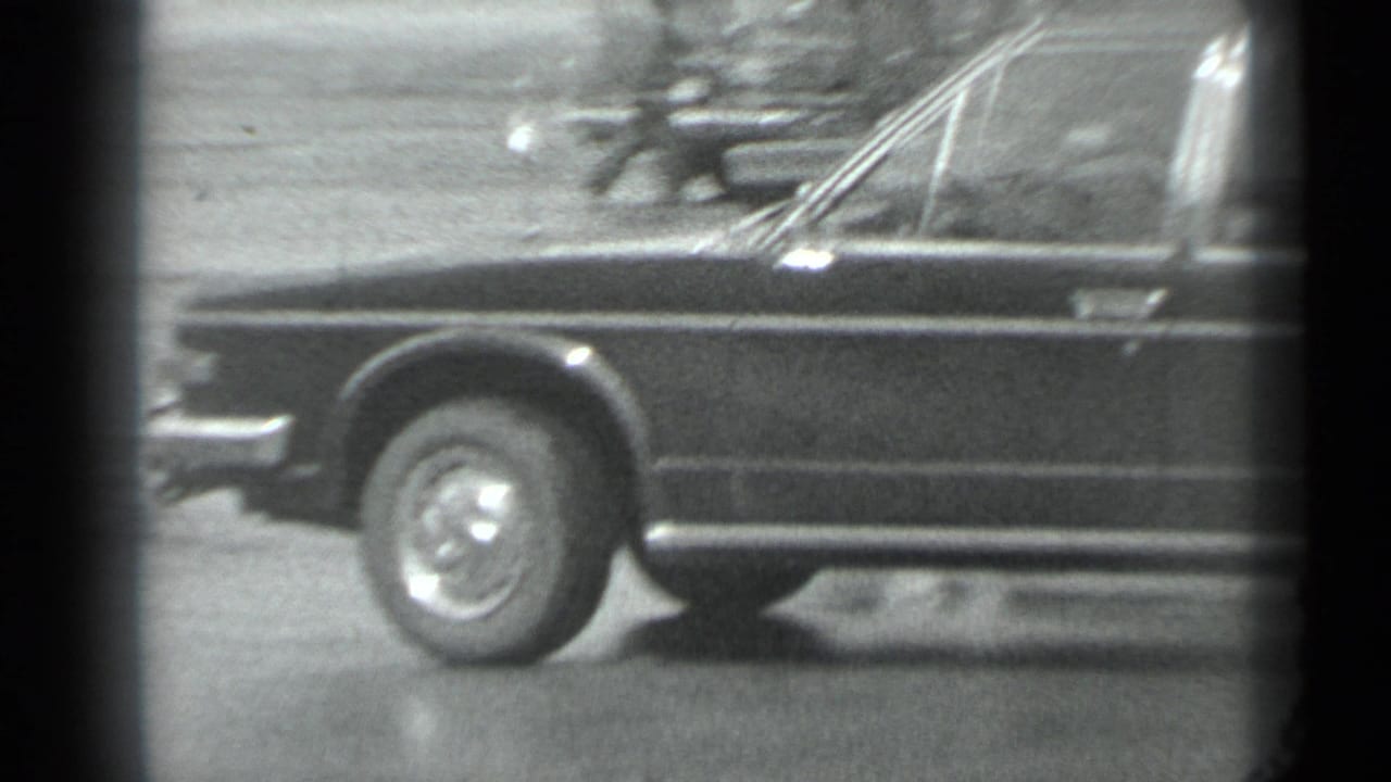 1983 Moscow 8mm frame showing the front side of a dark stretch car, including windshield, wheel, and chrome detailing.