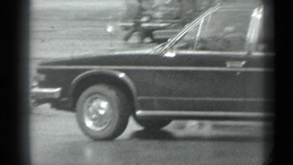 1983 Moscow 8mm frame showing the front side of a dark stretch car, including windshield, wheel, and chrome detailing.
