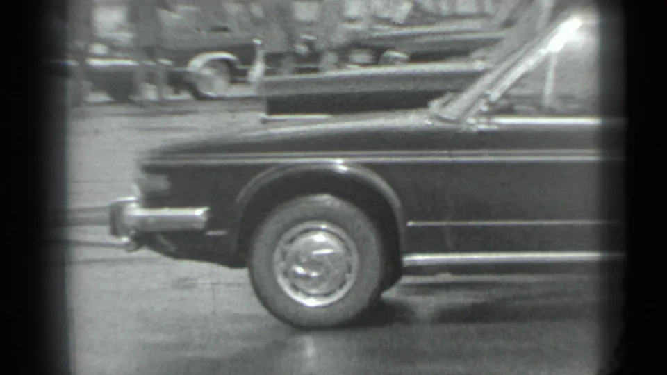 1983 Moscow 8mm frame with a close side view of the dark car, its chrome wheel, and another vehicle in the background.