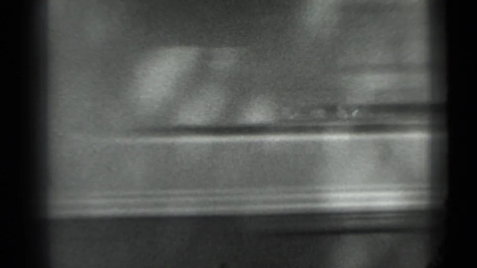 A soft, blurred 8mm frame shows the foreground car or obstruction passing close to the lens, with little identifiable detail.