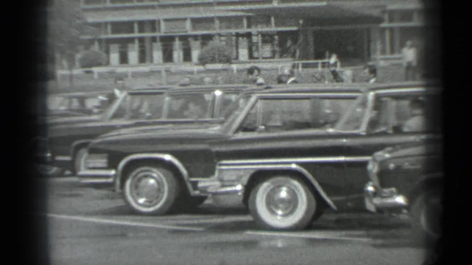 1983 Moscow street view with a dark station wagon in the foreground and suited men near a building behind it.