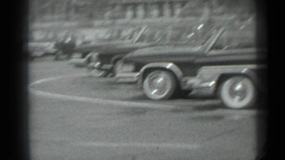 Motion-blurred 8mm frame from the 1983 Moscow clip, with a dark car crossing the view and people faintly visible behind it.