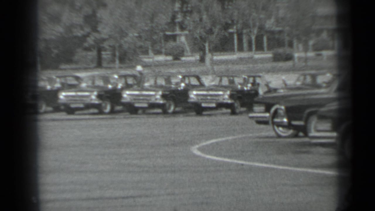 Parked sedans beside a broad street with motorcycle officers partly visible.
