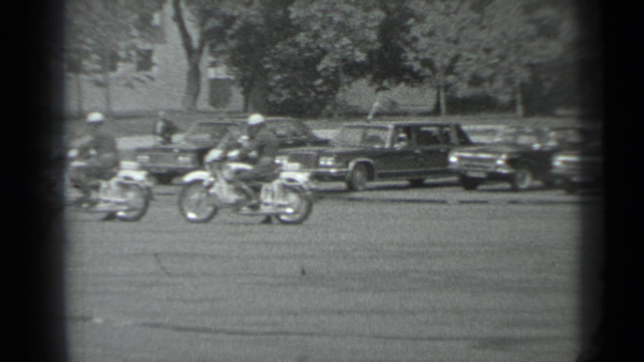 Motorcycle officers in white helmets move through a Moscow street with parked official cars in the background.