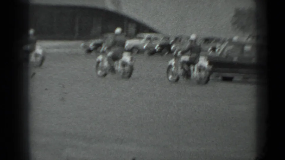 Motorcycle police with sidecars continue across an open Moscow street, with cars and a large building behind them.