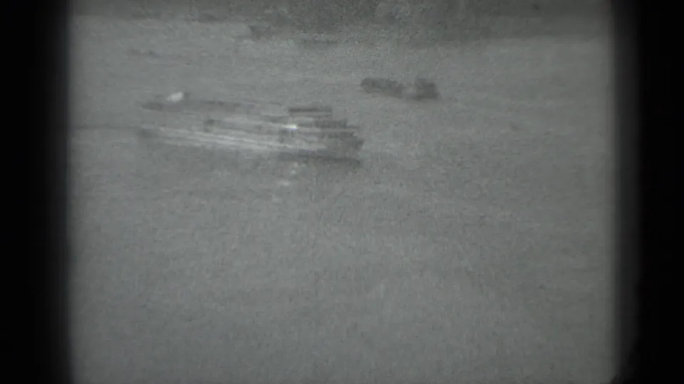 Grainy black-and-white frame looking toward pavement or park ground, with small indistinct objects near the center.