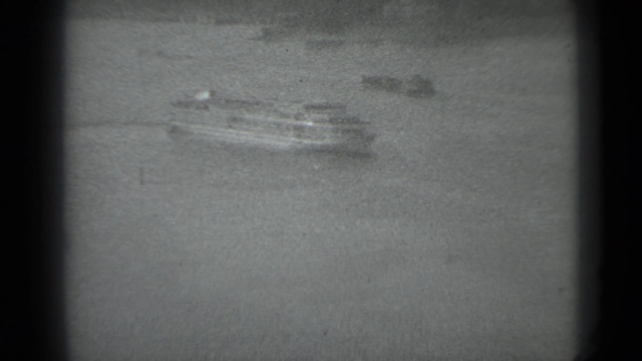 Small ferry boat visible across the river through grain and soft focus.