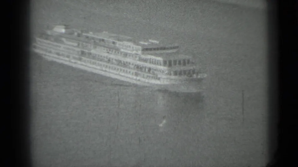 1983 Moscow home-movie frame showing a distant multi-deck passenger ship on calm water, seen through dark 8mm frame edges.
