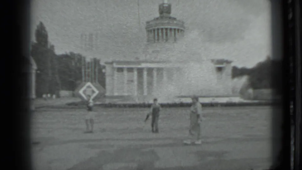 1983 Moscow 8mm frame showing a domed classical building beyond a lawn, with a few distant people standing or walking in the foreground.