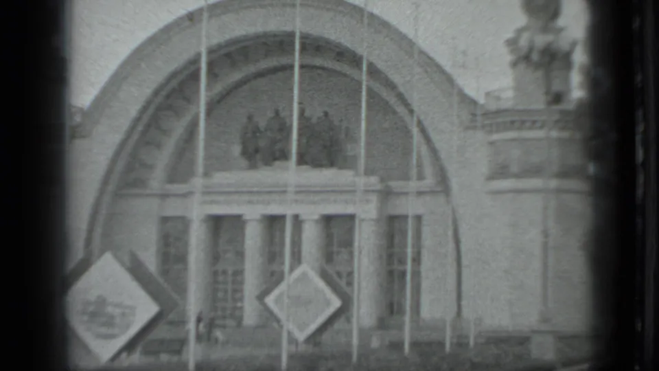 1983 Moscow 8mm frame focused on an ornate arched entrance with columns, flagpoles, sculptural figures, and diamond-shaped signs.