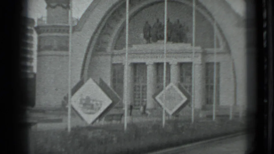 1983 Moscow 8mm frame showing a closer, slightly off-center view of the arched building entrance, columns, signs, and foreground grass.