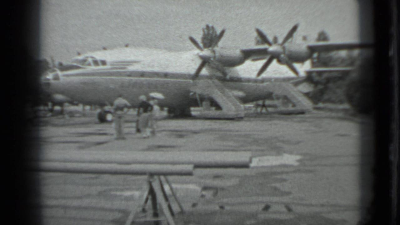 Large propeller aircraft on a tarmac with people nearby and a pipe-like barrier in the foreground.