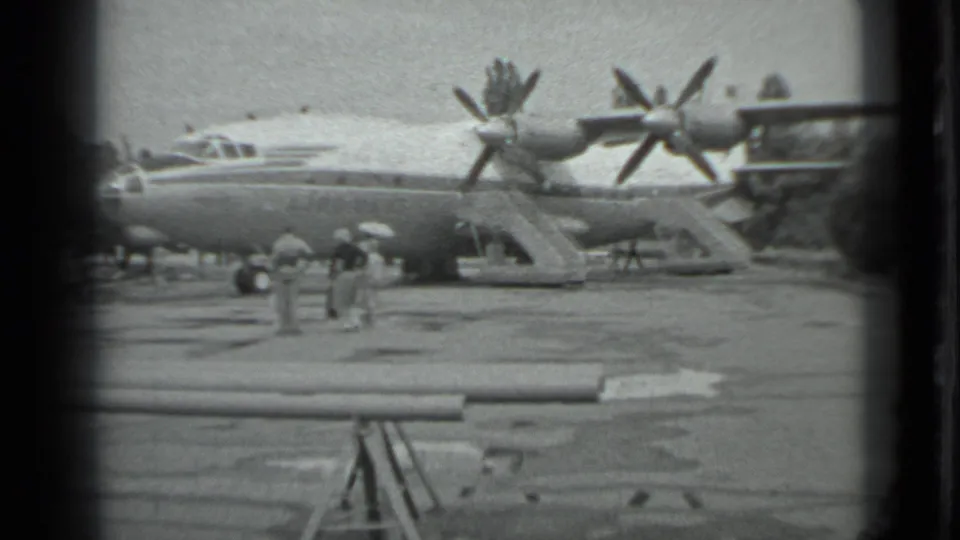 1983 Moscow 8mm frame showing a large propeller aircraft on the tarmac with several people nearby and dark film borders.