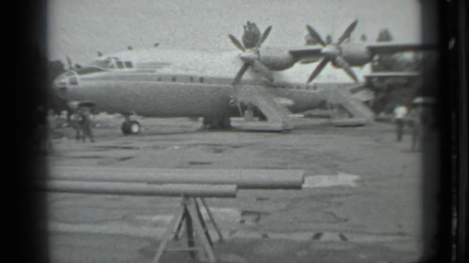 Side view of a large propeller aircraft at a Moscow airport in 1983, with distant people standing on the tarmac.