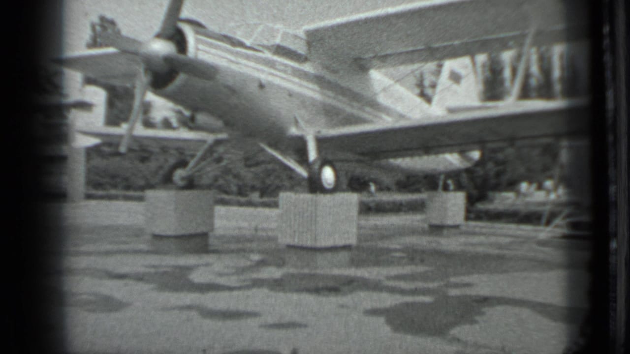 Twin-engine aircraft display seen from the side with wet pavement in front.