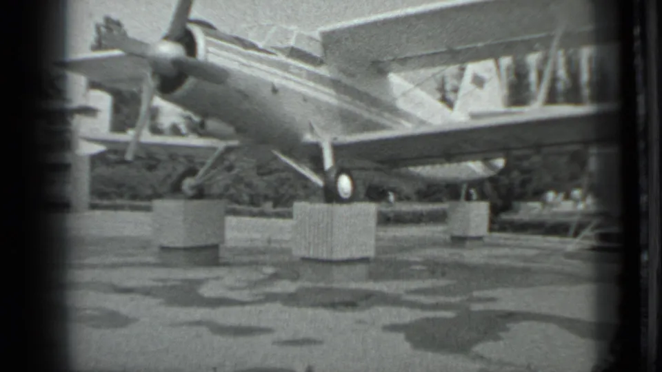 1983 Moscow 8mm frame showing a Soviet-marked twin-engine aircraft on concrete supports in a public outdoor display.