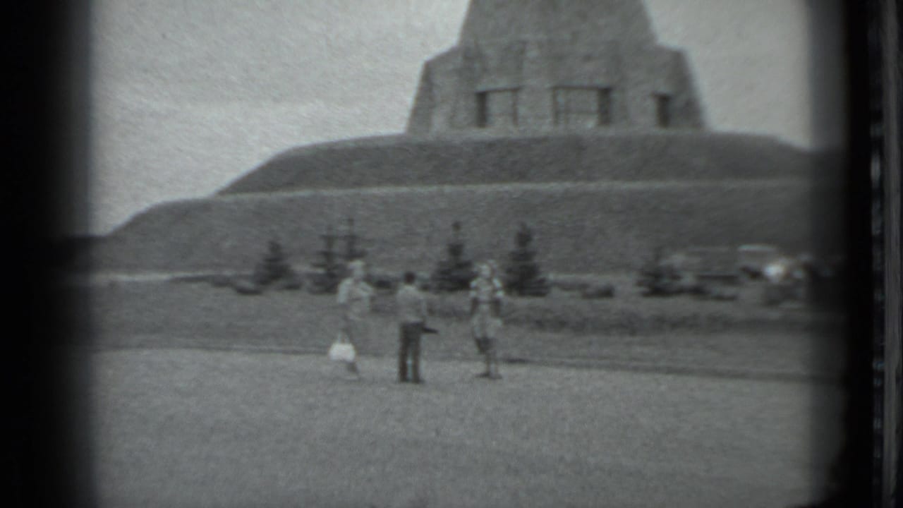 A small group stands on open ground below a stepped concrete structure.