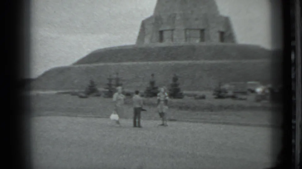 Three adults appear in the foreground below a large stepped concrete structure in Moscow, with trees and cars behind them.