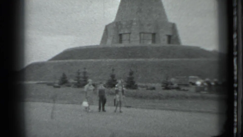 A 1983 Moscow visitor shot frames three adults below a broad concrete monument, with parked cars and trees in the background.