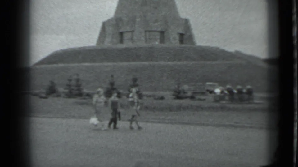 1983 Moscow frame of three visitors walking on grass below the pyramid-shaped monument, with parked cars in the background.