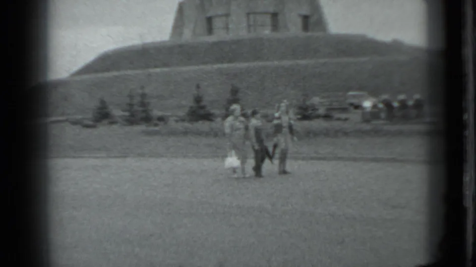1983 Moscow frame showing the walking group farther across the lawn, with the pyramid-shaped hillside monument in the background.