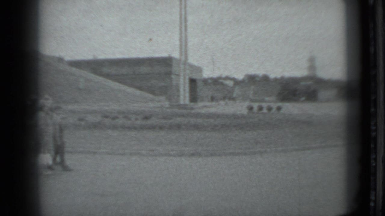 Distant visitors appear near a massive sloped concrete landmark form in Moscow, with open pavement and vertical poles in view.