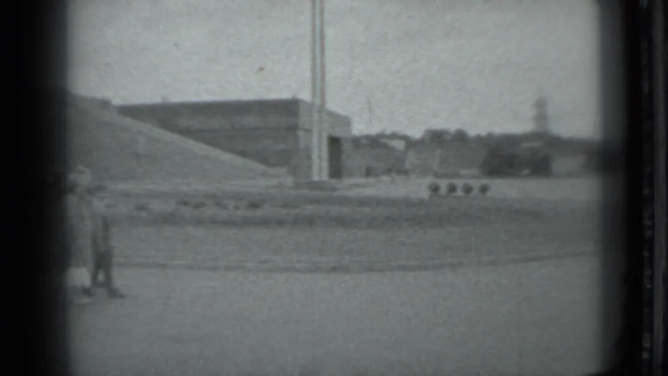 Distant visitors appear near a massive sloped concrete landmark form in Moscow, with open pavement and vertical poles in view.
